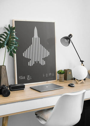Framed minimalist artwork of the F-22 Raptor, featuring bold graphic lines and Morse code typography. Screenprinted in metallic silver ink, displayed in a modern home office setting.